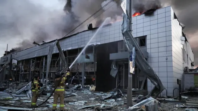 空爆を受けた店舗の屋上部分に炎が見え、消防士が消火活動をしている