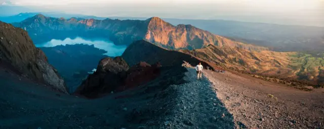 Foto Panorama Seorang Turis di Puncak Gunung Rinjani yang Berketinggian 3.726 m saat Matahari Terbit, Indonesia, Asia.