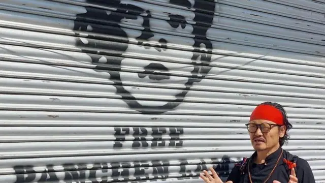 Aktywista i wyznawca Tenzin Tsundue stoi przed wizerunkiem Panczenlamy namalowanym na okiennicy sklepu.