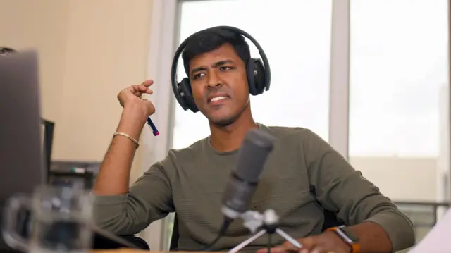 මේසයක් ඉදිරිපිට වාදී වී සිටින තරුණ පිරිමි ළමයෙක්  