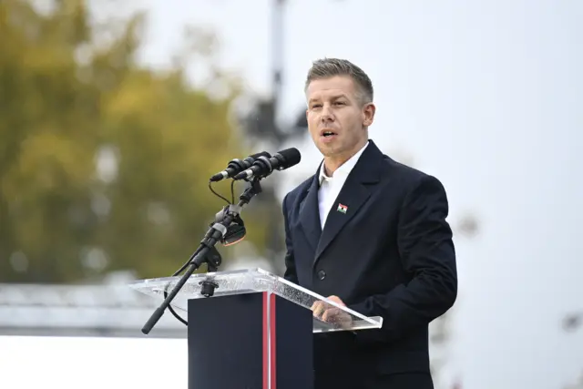 Петер Мадьяр в белой рубашке и черном пиджаке возле трибуны с микрофоном