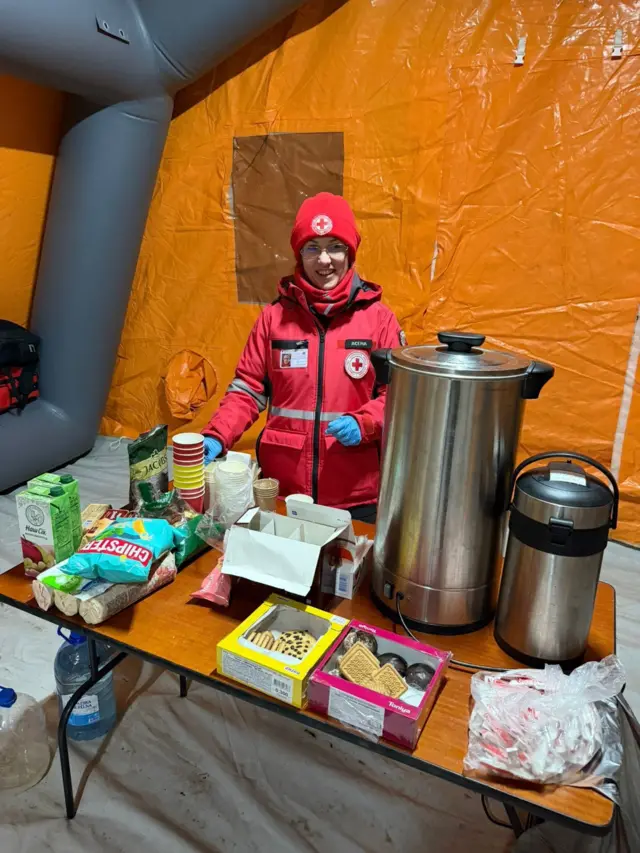 Дівчина стоїть за столом на ньому чай, кава, їжа 