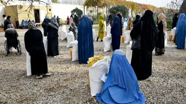 شماری از زنان افغان با چادری و برقه که خریطه‌های از کمک‌ها در مقابل شان قرار دارد.