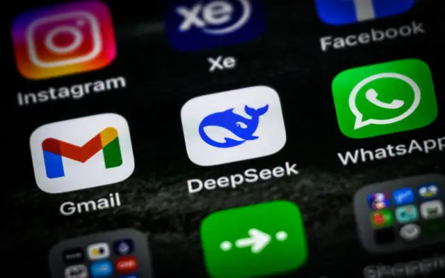 El logo de la aplicación DeepSeek, vista como se vería en un teléfono inteligente, junto a otras aplicaciones comunes. 