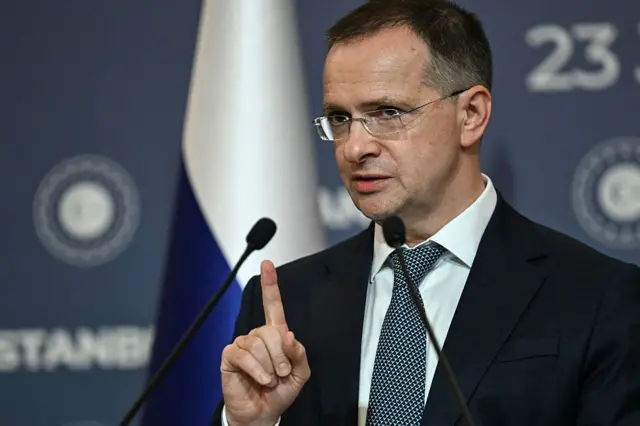 Мединский перед микрофоном, его указательный палец поднят вверх