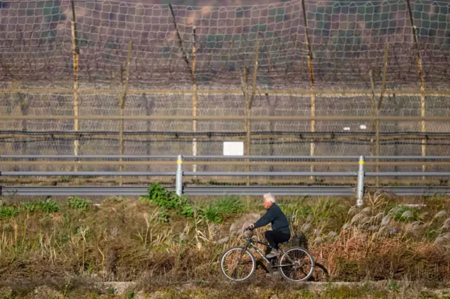 Na tym zdjęciu z 7 listopada 2024 r., mężczyzna jedzie na rowerze wzdłuż ogrodzenia granicznego na południowokoreańskiej wyspie granicznej Ganghwa