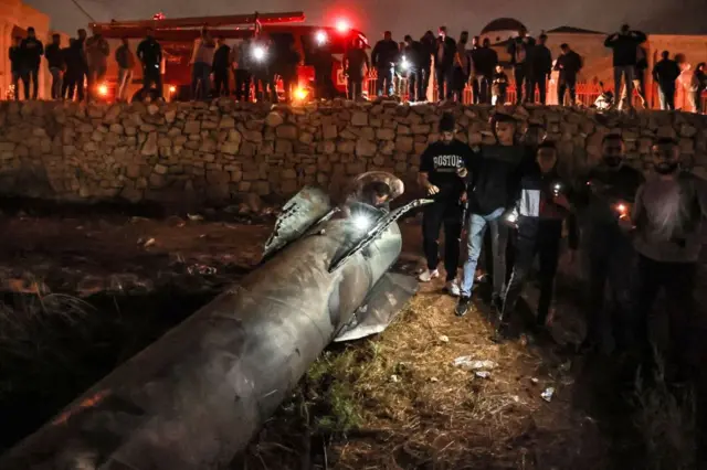 Em foto noturna, jovens observam e inspecionam míssil caído 