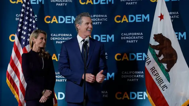 Гэвин Ньюсом (справа) выступает, а его жена Дженнифер Сибел Ньюсом (слева) наблюдает за ним во время собрания в штаб-квартире Демократической партии Калифорнии в ночь выборов 4 ноября 2025 года в Сакраменто, Калифорния. 
