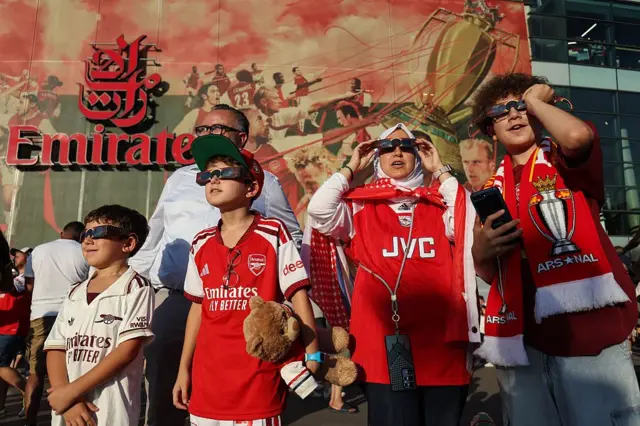 Aficionados del Arsenal observan el eclipse solar antes del partido amistoso de pretemporada entre el Arsenal FC y el Como Calcio en el Emirates Stadium, en Londres.