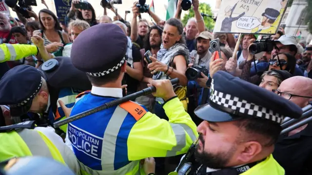 Полицейские, один из них с занесенной дубинкой, стоят напротив демонстрантов и фотографов
