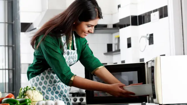 মাইক্রোওয়েভ ওভেনে রান্না করছেন এক নারী