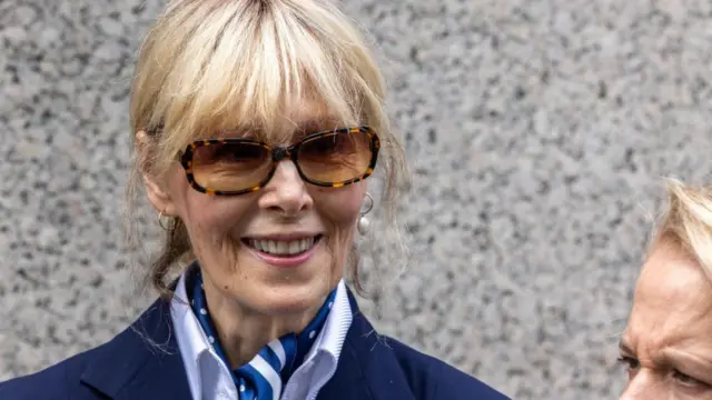 紺色のジャケットを着て茶色のサングラスをかけた金髪の女性が、笑顔を見せている