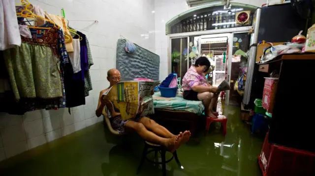 Duas pessoas lêem jornais dentro de uma casa inundada em Bangkok, perto do rio Chao Phraya, em 16 de outubro de 2011