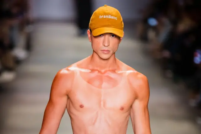 Modelo sem camisa desfila com boné na São Paulo Fashion Week