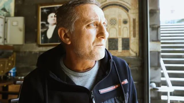 Mavi gözlü bir adam, arkasında Atatürk resmi