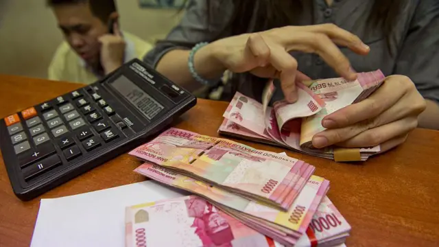 Seorang karyawan di tempat penukaran uang menghitung uang rupiah.