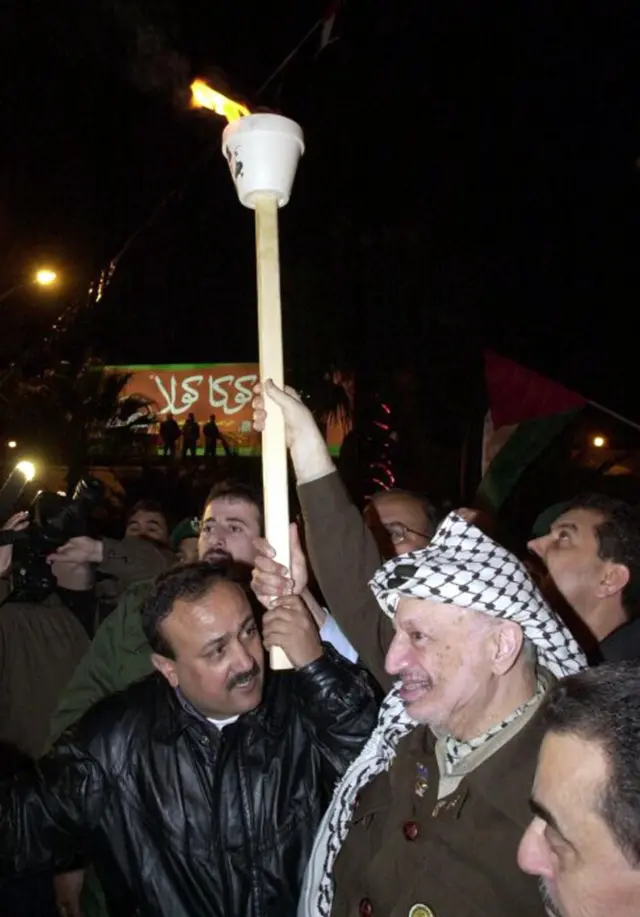 صورة أرشيفية تجمع بين الزعيم الفلسطيني الراحل ياسر عرفات (يمين) والقيادي الفلسطيني مروان البرغوثي (يسار)، يحملان شعلة خلال مسيرة نظمتها حركة فتح لإحياء الذكرى 37 لميلادها - 2001