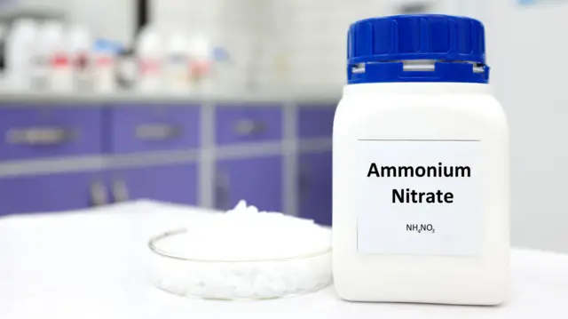یک بطری نیترات آمونیوم در یک بطری پلاستیکی در کنار یک ظرف با گلوله های سفید در داخل یک زمینه آزمایشگاهی. ماده شیمیایی مورد استفاده برای کود و مواد منفجره.