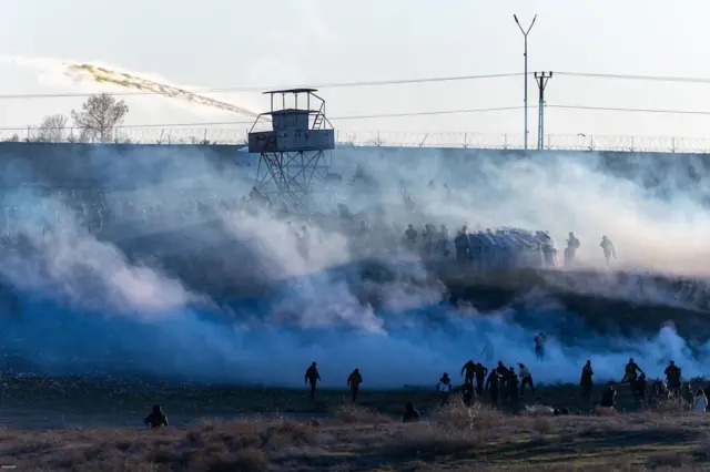 Suriyeli Kürtlere destek amacıyla düzenlenen yürüyüş sırasında, Kürt yanlısı protestocular Kamışlı'ya yürümeye çalışırken Türk polisiyle çatıştı. Alanda yükselen duman arasında protestocular seçiliyor. Bir de gözetleme kulesi var. Gösteri, Mardin'in Nusaybin ilçesinde gerçekleşti. 20 Ocak 2026. 