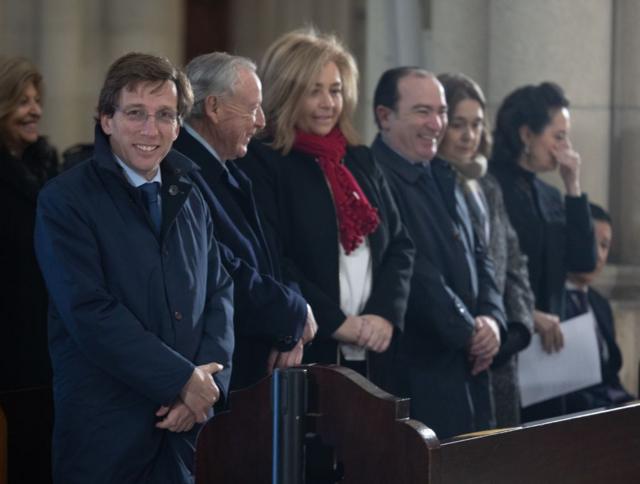 El alcalde de Madrid mira sonriente a la cámara desde el banco de una iglesia.  en una misa