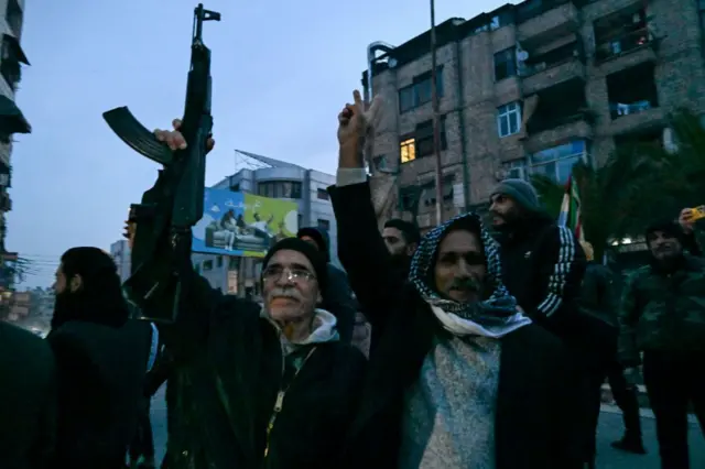 سكان محليون يتجمعون في أحد شوارع جرمانا، أحدهم يحمل سلاحاً رشاشاً، ضاحية دمشق، في 8 ديسمبر/كانون الأول 2024 عقب سقوط بشار الأسد