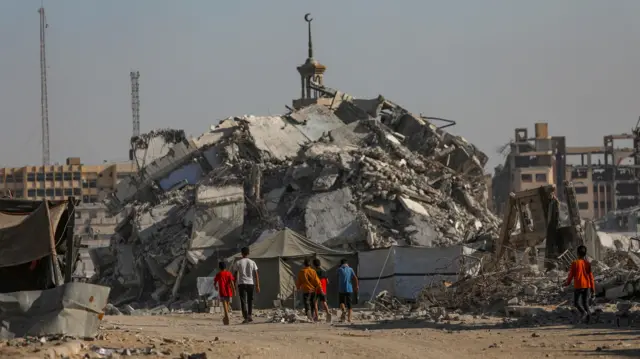 Gazze'de yıkılmış bir binanın önünde yürüyen çocuklar