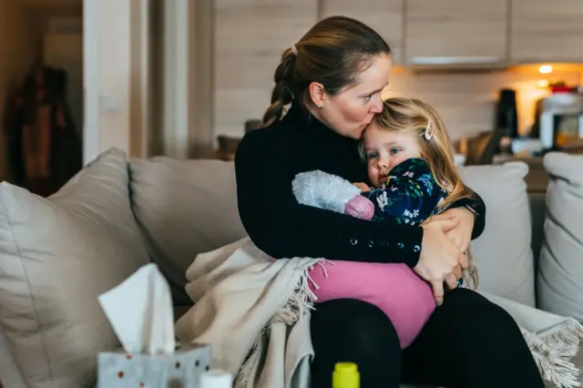 Mãe abraçando a sua filha no sofá de casa