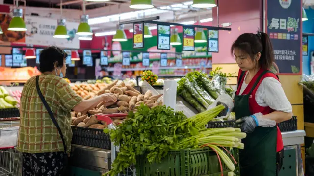 An elderly woman buys vegetables in a market in Beijing, China