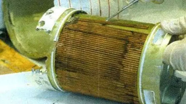 Крупний план циліндричного металевого елемента, розрізаного вздовж, із відкритою внутрішньою частиною. Всередині видно густо складену коричневу гофровану вставку — фільтрувальний матеріал, покритий брудом і темними смугами.