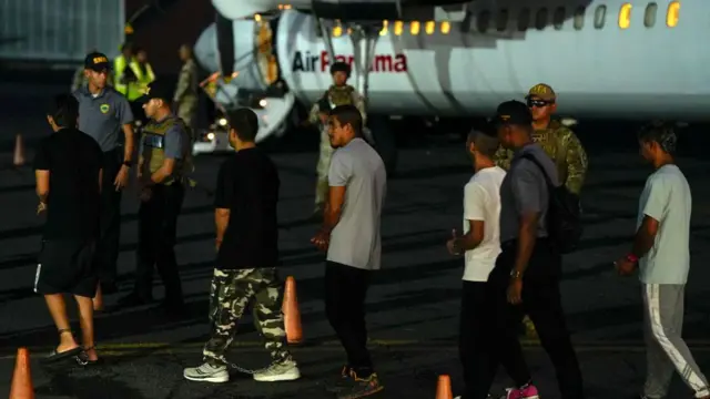 Migrantes colombianos, con las manos y los pies esposados, hacen fila para subir a un avión en el aeropuerto Albrook Gelabert de la ciudad de Panamá el 20 de agosto de 2024, durante su deportación.