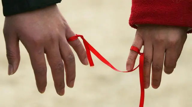 Двоє людей з пов'язаною червоною стрічкою на мізинцях