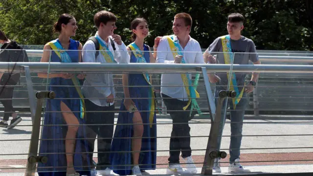 Випускники школи, дівчата та хлопці в урочистому вбранні й синьо-жовтих стрічках стоять на мосту. Архівне фото. 