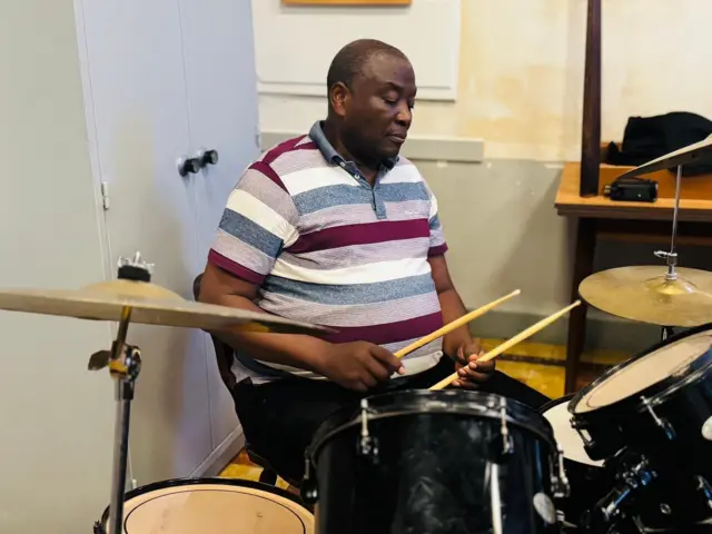 Kirokiro afashe imirisho yicaye ku gatebe, imbere yiwe hari ingoma zibiri yunamye aziraba, hirya i bumbafu hari simbale, iyindi i buryo