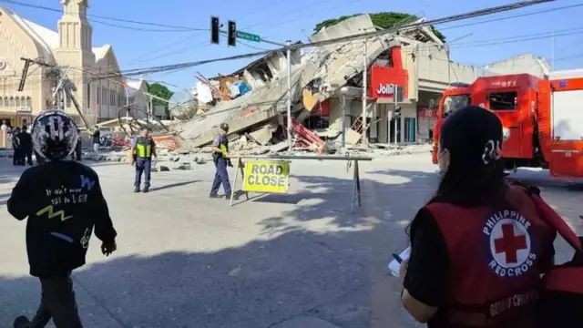 Sejumlah polisi dan Tim SAR berkumpul di depan restoran cepat saji Jollibee yang runtuh setelah gempa berkekuatan 7,7 magnitudo mengguncang Kota General Santos, di selatan Filipina, Senin (08/06). 