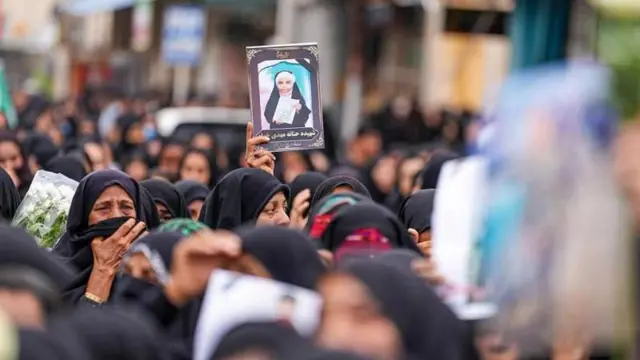 Siyah çarşaflı kadınlar kız okulu cenazesinde bir aradalar, kalabalıktan yükselen en çocuklardan birinin resmini havaya kaldırıyor. 