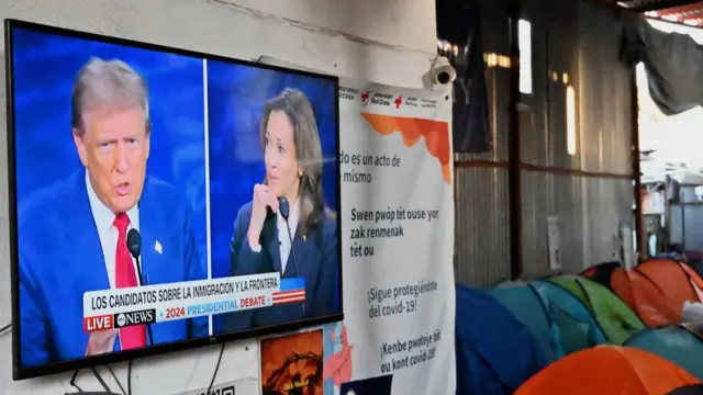 O primeiro debate entre Kamala Harris e Donald Trump é exibido em uma televisão no abrigo Juventud 2000 em Tijuana, México, ao lado de barracas coloridas