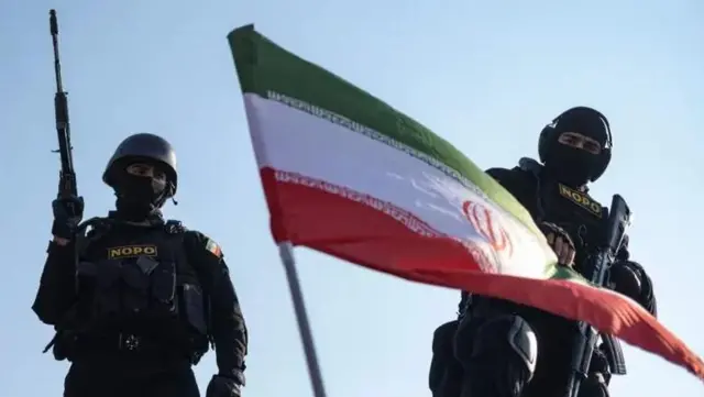 دو نیروی امنیتی «نوپو» با چهره‌های پوشیده و مسلح و پرچم جمهوری اسلامی در جلوی آنها