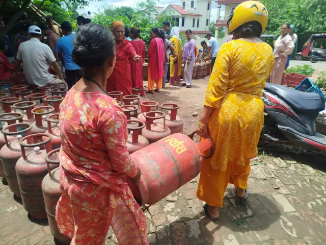 ग्यासका लागि लामबद्ध मानिसहरू र सिलिन्डर बोक्दै महिला