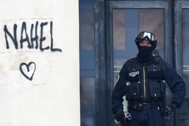Oficial de la policía nacional francesa asegura la entrada a un edificio junto al nombre 'Nahel', rociado en una columna durante las protestas en Nantes, en el oeste de Francia, el 30 de junio de 2023.