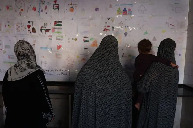 نساء يتأملن مجموعة من الرسومات التي رسمها أطفال في إحدى مدارس النزوح
