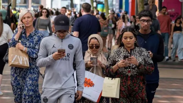 ثلاثة أجيال من عائلة يمشون عبر الطريق وهم ينظرون إلى هواتفهم.
