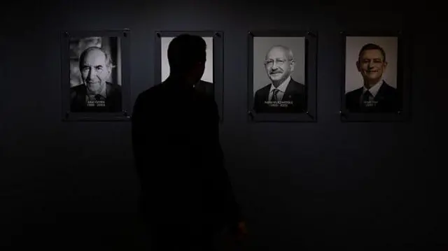 Bir kişi parti genel merkezinde eski CHP liderleri Altan Öymen ve Kemal Kılıçdaroğlu’nun ve mevcut lider Özgür Özel’in fotoğraflarının önünden geçiyor.Karanlık ve silüeti görünüyor. 