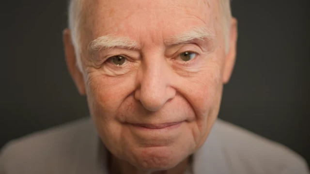 Gros plan sur le visage souriant d'un homme aux cheveux gris et aux sourcils gris. 