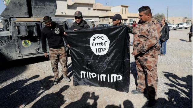جنود من الجيش العراقي يحملون علماً مقلوباً رأساً على عقب لتنظيم الدولة بالقرب من قاعدة عسكرية خارج مدينة الموصل