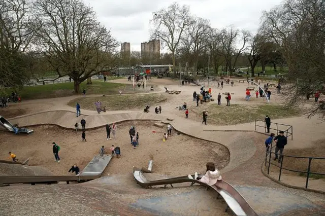 Kumluk alana entegre edilmiş bir çocuk parkı. Etrafta ağaçlar.
