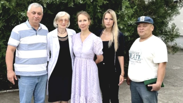 Diversas pessoas brancas posam para foto, uma mulherbet 365 cs govestido lilás claro está no centro