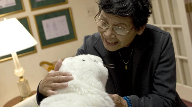 一人正在和外形像小海豹的机器人Paro说话