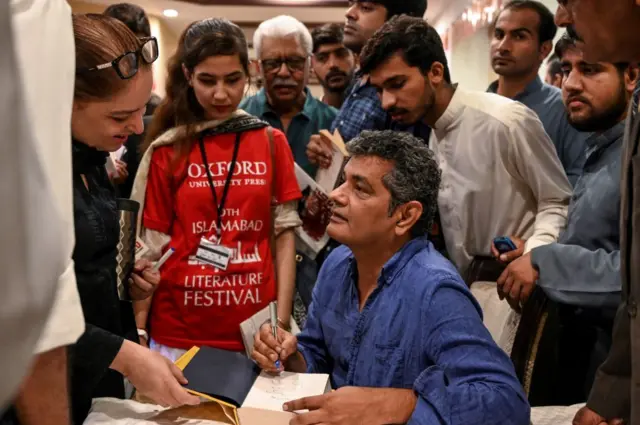 পাকিস্তানে একটি সাহিত্য অনুষ্ঠানে নিজের বইতে পাঠকদের সই দিচ্ছেন মোহামেদ হানিফ