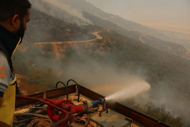  صورة تظهر رجل إطفاء يعمل على إخماد الحرائق بعد اندلاع حريق هائل في حماة بسوريا في 13 أغسطس/آب 2025.