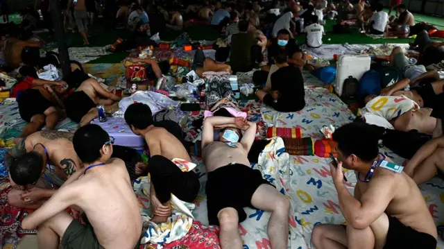 በተጨናነቀ የመጠለያ ክፍል ውስጥ ያሉ እና ከወገባቸው በላይ እርቃናቸውን የሆኑ ወንዶች ጨርቅ በተነጠፈበት ወለል ላይ ተኝተው